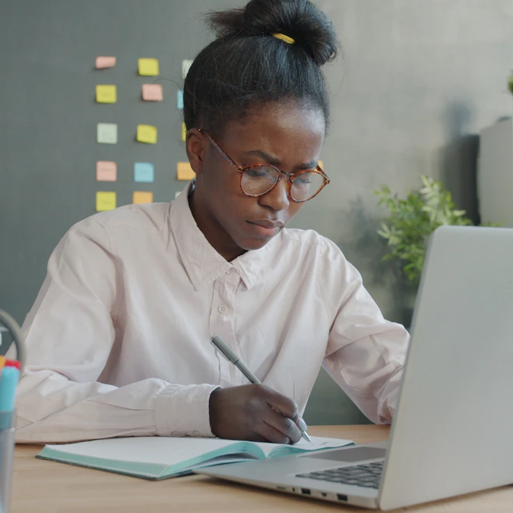 Professional taking notes beside a laptop in a modern office